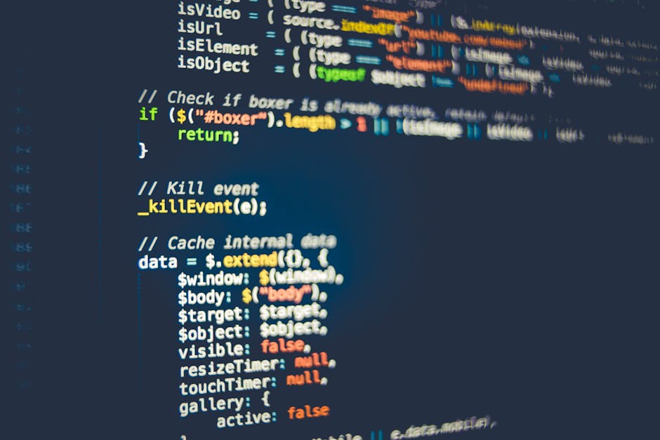 The image shows a close-up of a person's hand typing on a silver laptop keyboard, placed on a wooden surface. The laptop screen displays lines of code, indicating programming or web development work. 